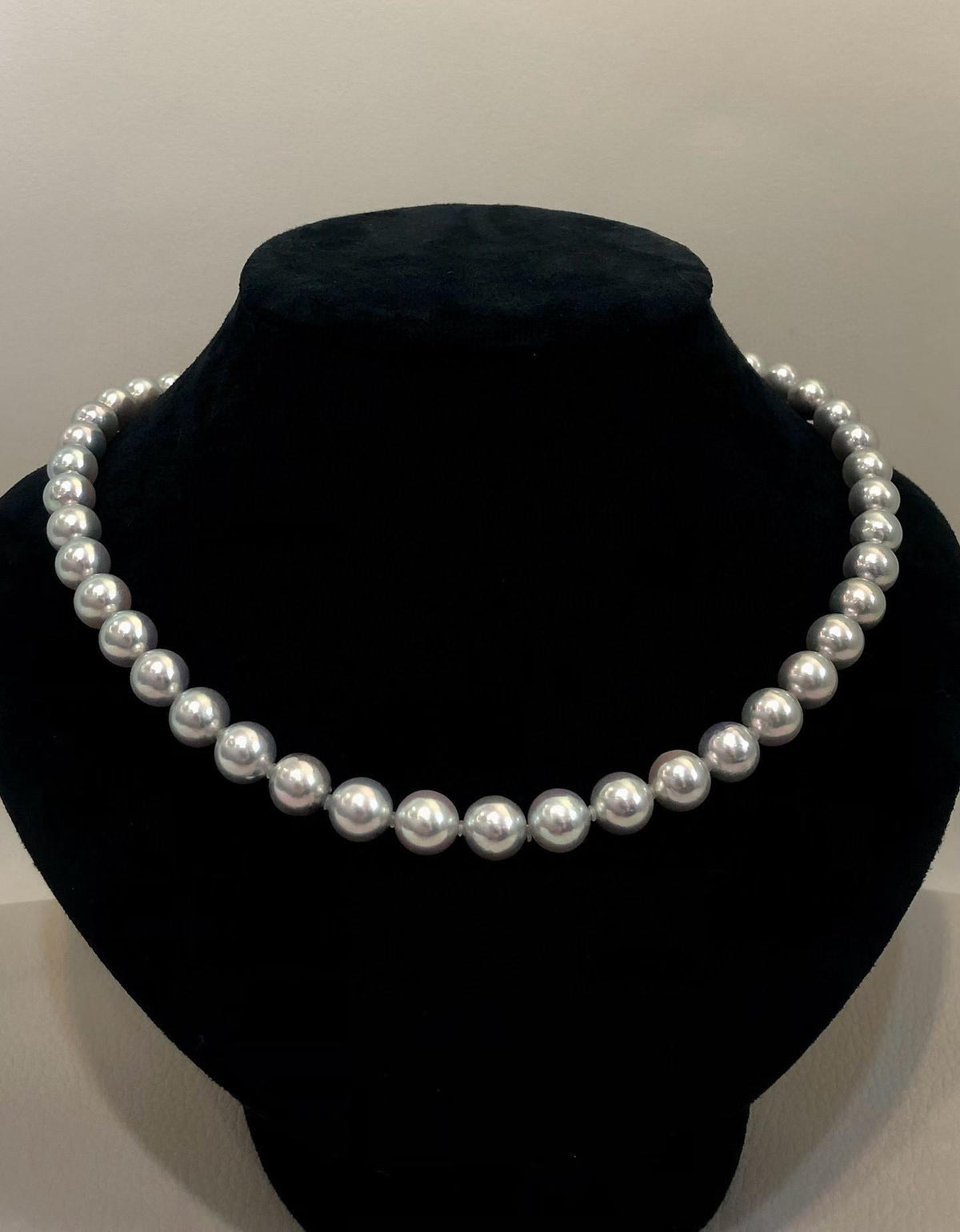 A classic strand of white freshwater pearls displayed on a black velvet jewelry bust against a neutral light gray background.