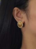 A close-up of a person's ear wearing a gold crescent moon stud earring with a halo of small clear stones.