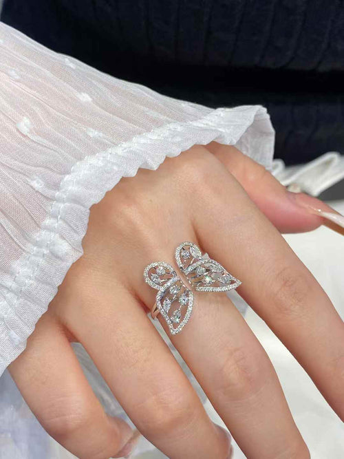 A silver butterfly ring with clear stones, worn on a hand with a white ruffled sleeve and a dark ribbed sweater in the background.