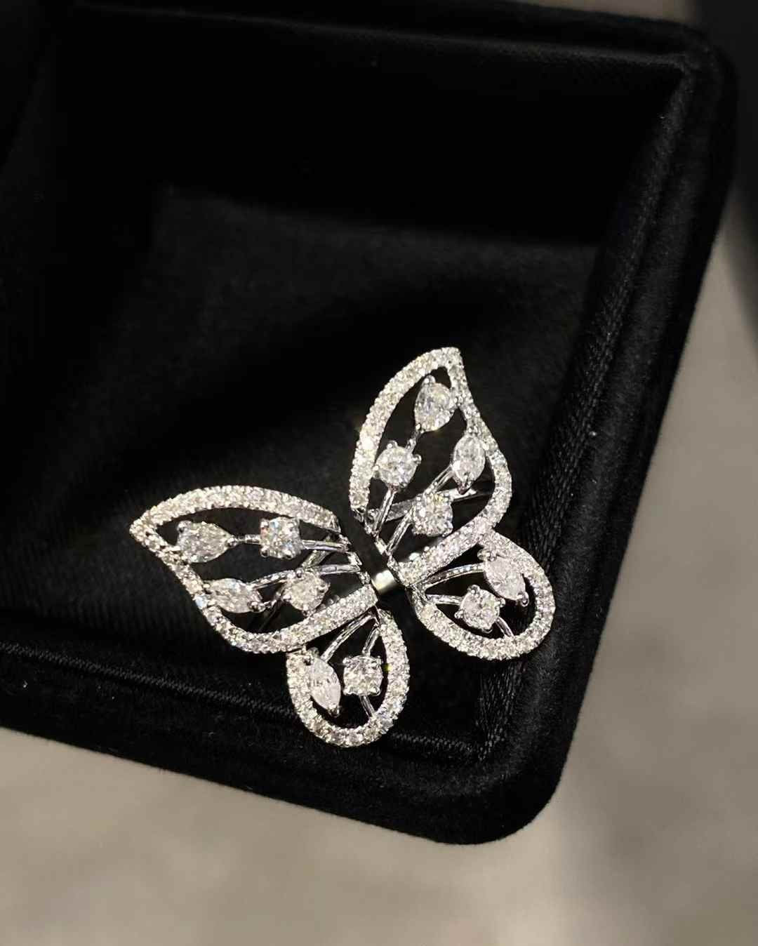 A silver butterfly-shaped brooch adorned with pavé-set clear stones, displayed on a black velvet jewelry box.