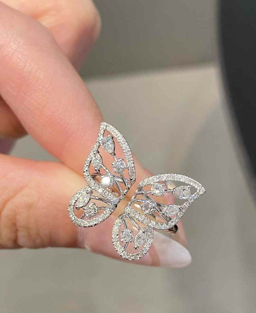 A close-up of a hand holding a butterfly-shaped silver ring adorned with sparkling clear gemstones.