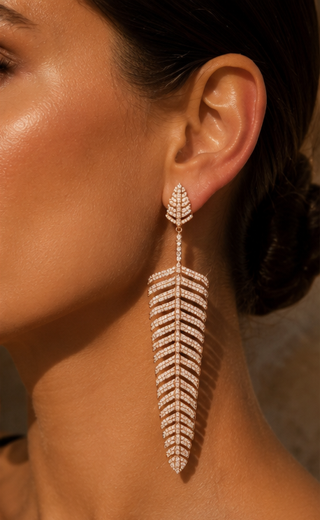 A close-up lifestyle shot of a model wearing a large, feather-shaped drop earring adorned with sparkling clear stones in a rose gold setting.