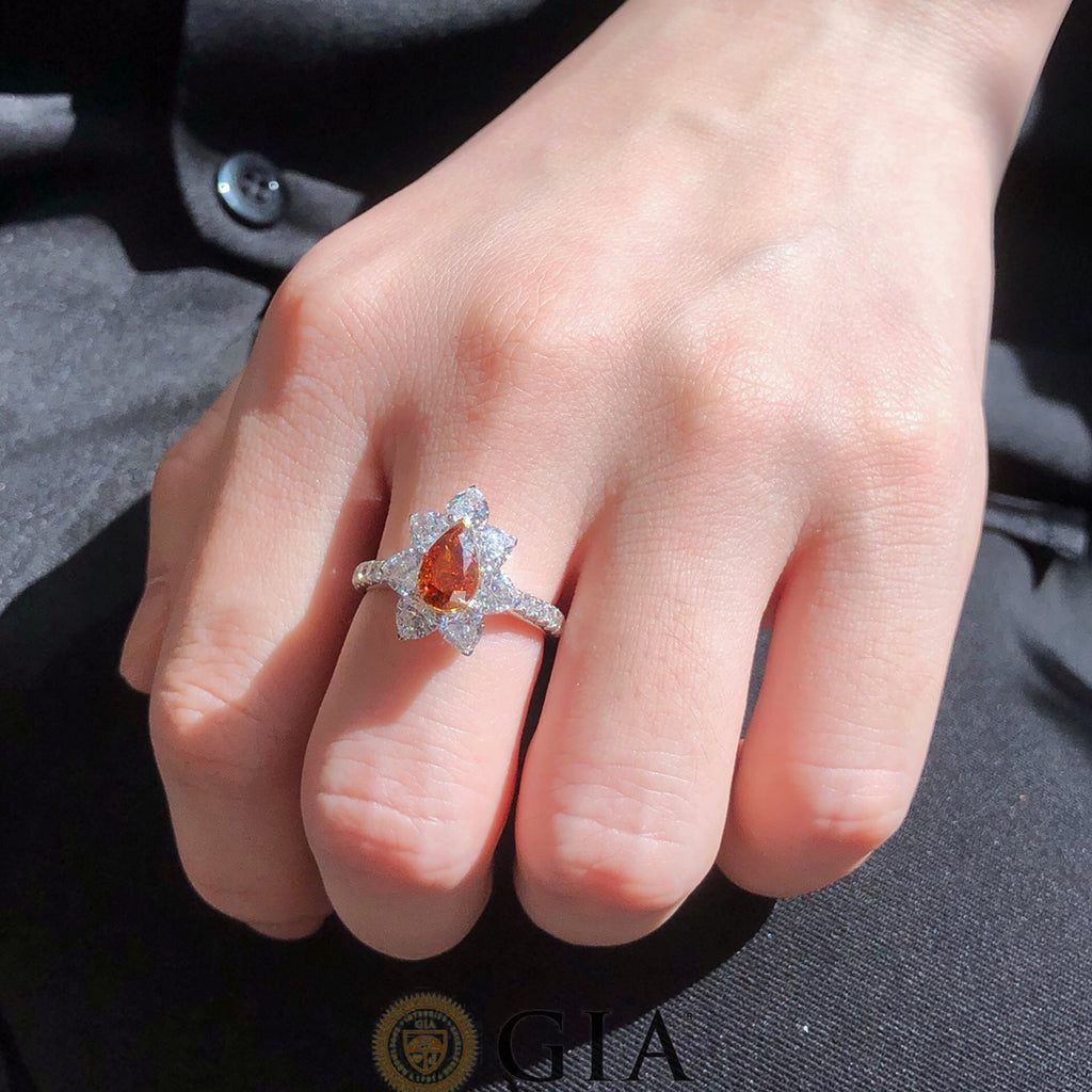 Close-up of Fancy Deep Orange Brownish Pear Diamond center stone with white diamond accents in 18k gold