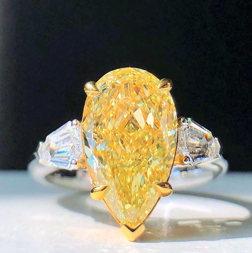  Close-up of GIA fancy yellow pear cut diamond with surrounding white diamonds.