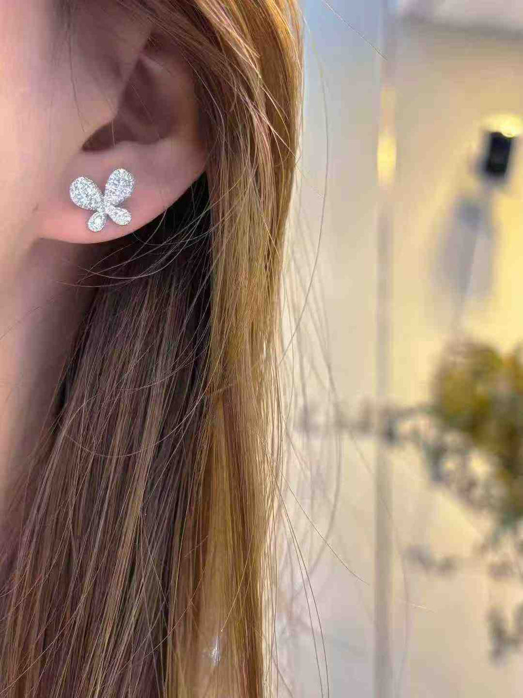 Close-up of a person wearing a silver butterfly earring with a blurred background