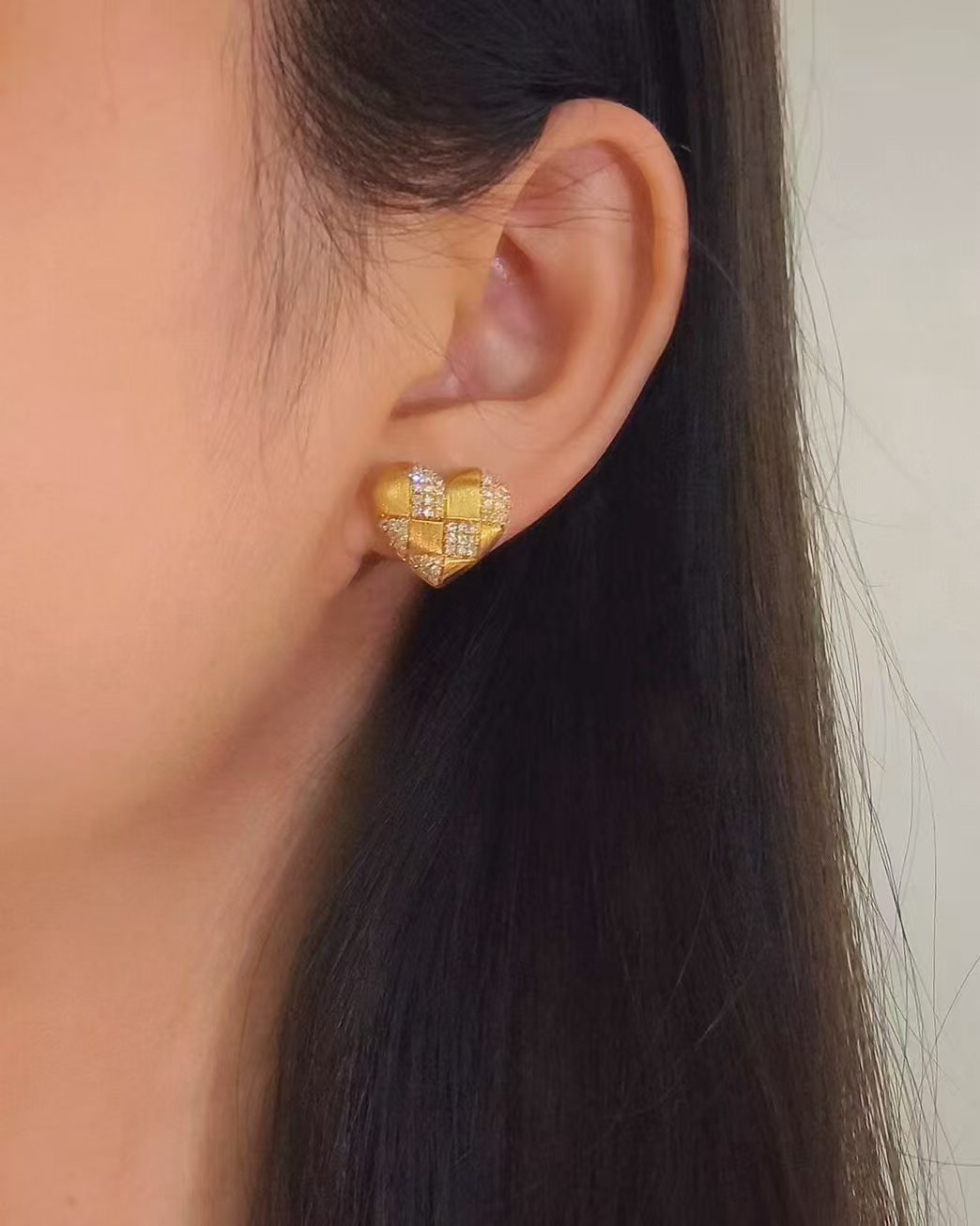 Heart-shaped gold stud earring with alternating brushed gold and diamond-set sections, shown worn on the ear. 